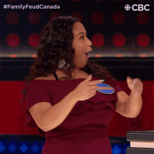 a woman in a red dress is clapping her hands in front of a sign that says family feud canada