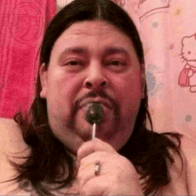 a shirtless man with long hair and a beard is eating a lollipop .