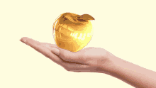 a woman 's hand is holding a golden apple on a white background