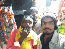 three men are posing for a picture with one wearing a yellow scarf and a beanie