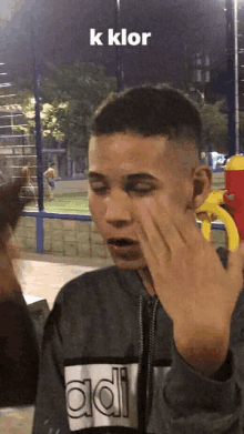 a young man wearing an adidas sweatshirt covers his face with his hand