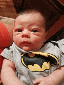 a baby wearing a batman shirt is being held by a person