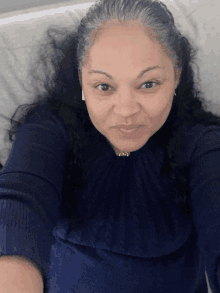 a woman in a blue sweater takes a selfie on a bed