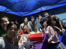 a group of people are posing for a picture under a blue canopy