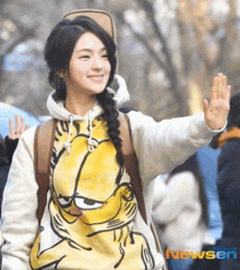 a girl wearing a garfield sweatshirt is waving at the camera