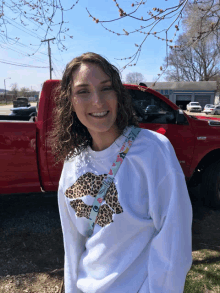 a woman wearing a white sweatshirt with a leopard print on it smiles in front of a red truck