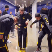 a group of basketball players are standing in a locker room and one of them is wearing a golden state warriors jersey .