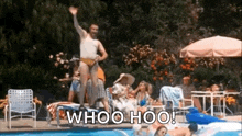 a man in a bathing suit is jumping into a swimming pool with a group of people sitting around it .