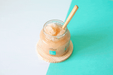 a jar of scrub with a wooden spoon in it sits on a wooden coaster