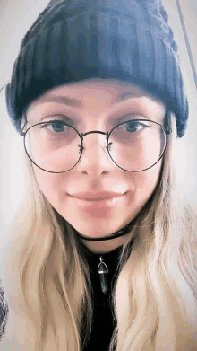 a woman wearing glasses and a beanie is smiling