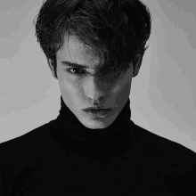 a man wearing a black turtleneck looks at the camera