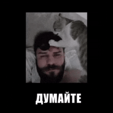 a man with a beard is laying in bed with a cat on his head