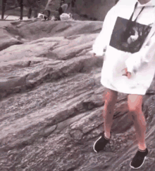 a person wearing a white hoodie and black shoes is walking on a rocky surface