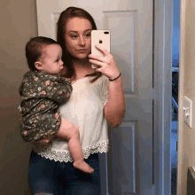 a woman is holding a baby and taking a selfie in front of a mirror