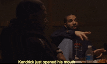 a man sitting at a table with a bottle of water and kendrick just opened his mouth