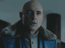 a bald man with blue eyes is wearing a blue leather jacket