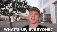 a young man standing in front of a building with the words " what 's up everyone " above him