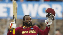 a cricket player is holding a bat and a helmet in his hands .