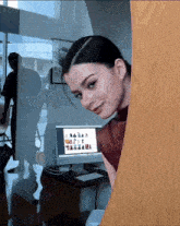 a woman peeking out from behind a wooden door looking at a computer monitor