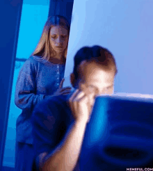 a woman stands behind a man looking at a computer monitor