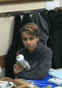 a boy is sitting at a table holding a bottle of glue .