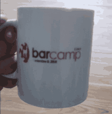 a person is holding a coffee mug that says barcamp on it