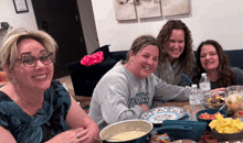 four women are sitting at a table with plates and bowls of food and one woman is wearing a sweater that says dodgers