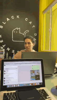 a woman sits at a desk with a laptop in front of a blackboard with the word black cat on it