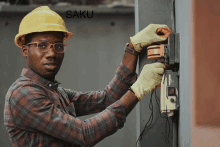 a man wearing a hard hat and gloves is working on an electrical box with the words " saku " in the background