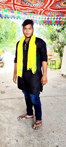 a man wearing a black shirt and a yellow scarf stands in front of a colorful tent