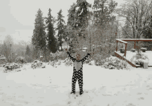 a little girl in a black and white polka dot pajamas is standing in the snow with her arms outstretched