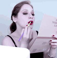 a woman is applying lipstick to her lips while looking at a book that says adam 's makeup palette