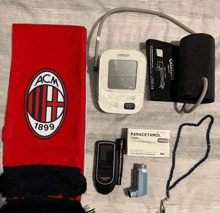 a scarf with the acm 1899 logo on it sits next to a blood pressure monitor