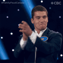 a man in a suit applauds while wearing a name tag that says ' family feud canada ' on it