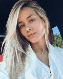 a woman with long blonde hair is wearing a white shirt and a necklace