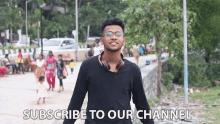 a young man with headphones around his neck stands in front of a sign that says subscribe to our channel