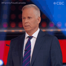 a man in a suit and tie is standing in front of a microphone with the words family feud canada above him