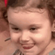 a little girl with a red bow in her hair is smiling and sticking her tongue out .