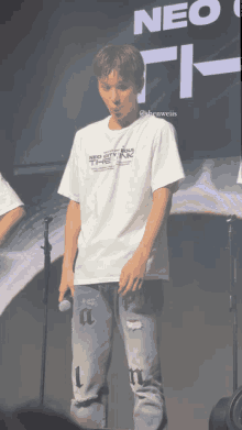 a man wearing a white neo city t-shirt stands on stage