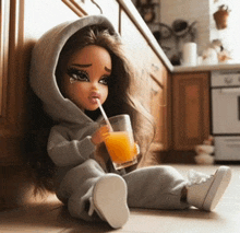 a doll is drinking orange juice through a straw in a kitchen