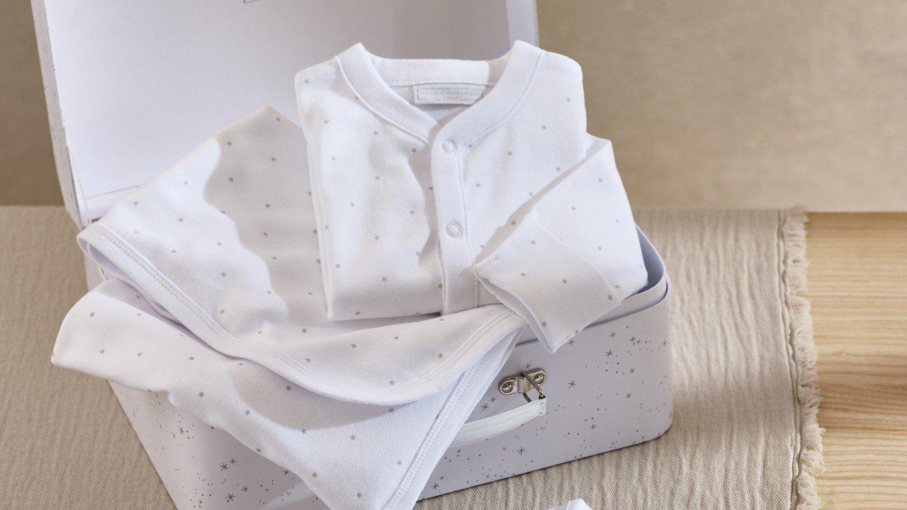 a white baby outfit is sitting in a suitcase on a table