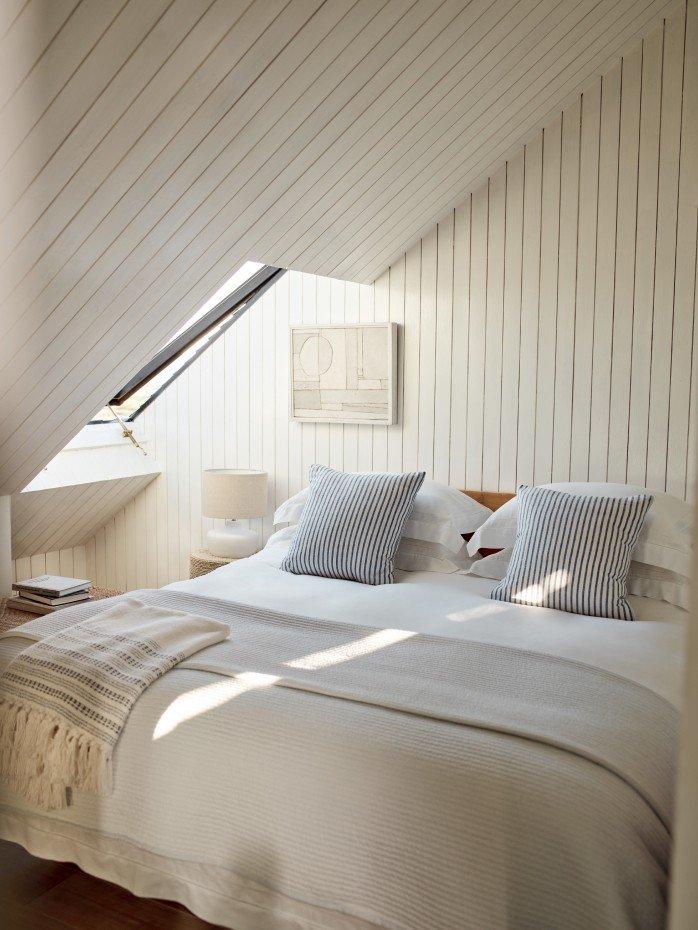 a bed with white sheets and pillows in a room with a skylight