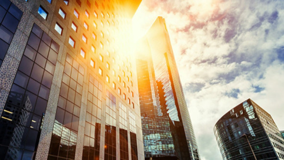 Skyscraper glass facades on a bright sunny day with sunbeams in the blue sky. Modern buildings in business district. Economy, finances, business activity concept. Bottom up view