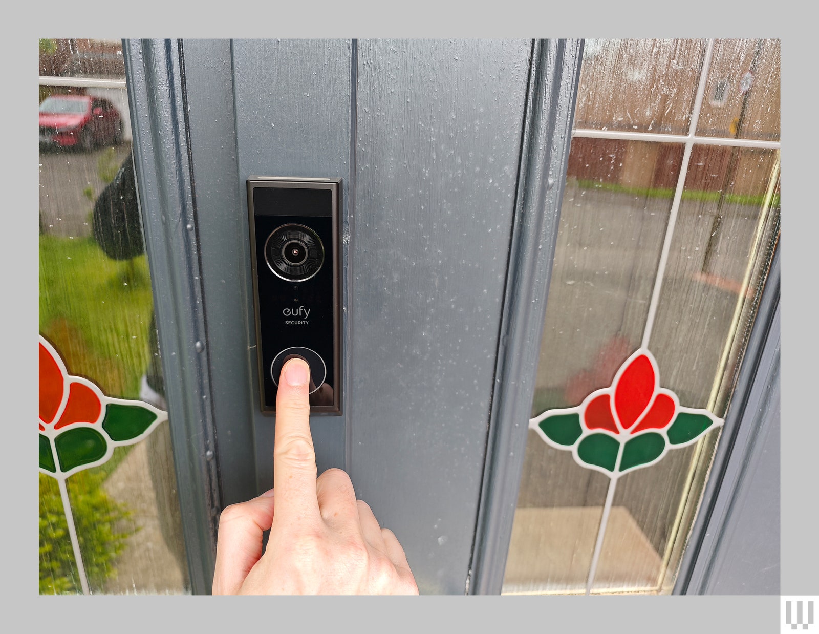 Bronze rectangular electronic doorbell with builtin camera attached to a grey door while a person pushes the main button