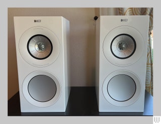 White rectangular speakers with 2 circular areas on each sitting on a dark wooden surface