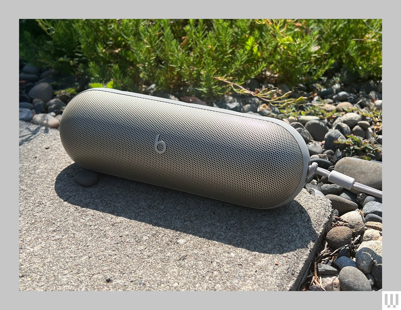 Oval shaped portable grey speaker on the corner of pavement by the grass