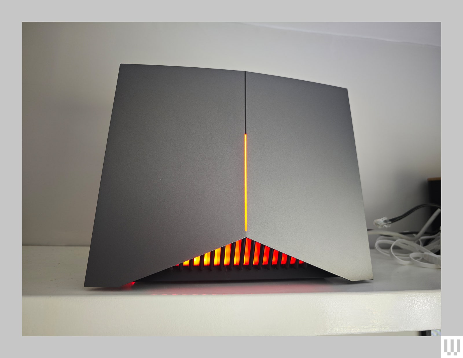 The TP Link Archer GE800 wifi router sitting on a shelf a black device with angular bottom and orange illuminated panels