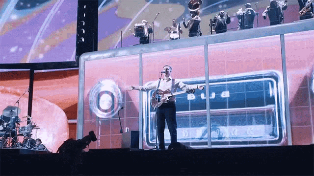 a man singing into a microphone on a stage with a large screen behind him that says ' blue '