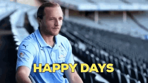 a man in a blue shirt is sitting in a stadium with the words happy days in yellow letters behind him