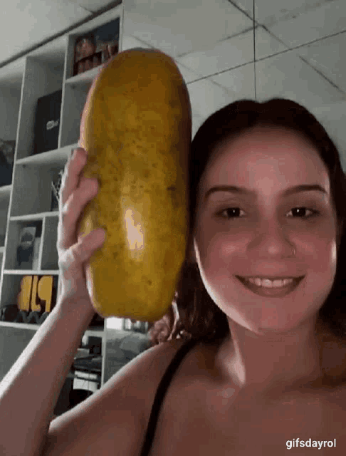 a woman is holding a very large yellow fruit in front of a shelf with the number 19 on it